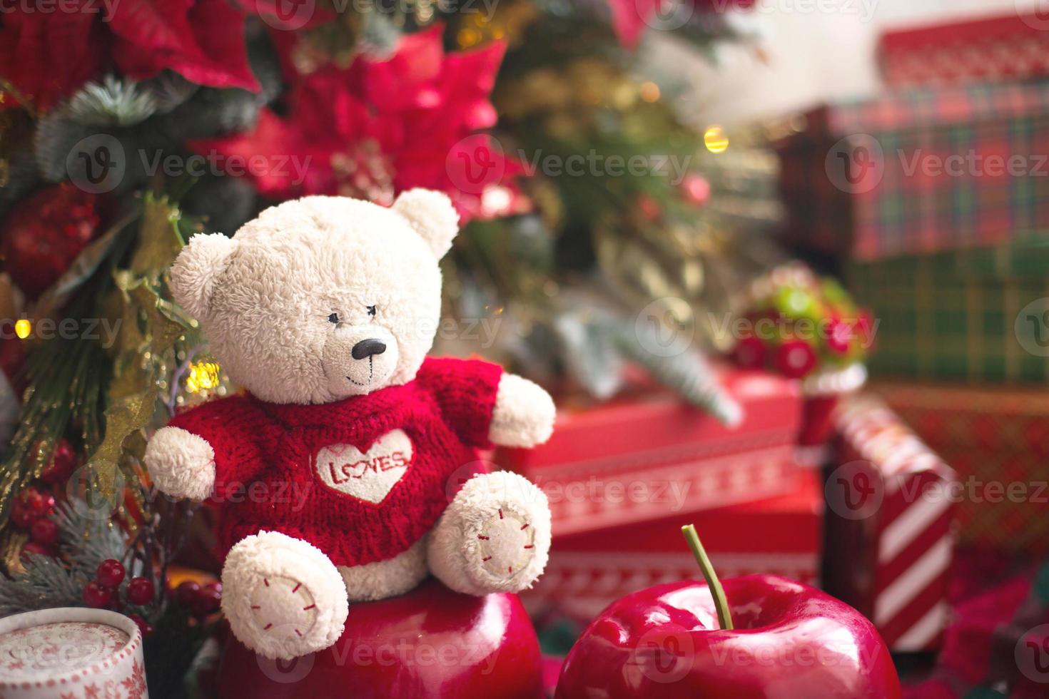 ours en peluche blanc en pull rouge avec coeur sur la poitrine et les mots amour près du sapin de noël parmi les coffrets cadeaux. cadeau à votre bien-aimé, déclaration d'amour, décor poinsettia. copie espace photo