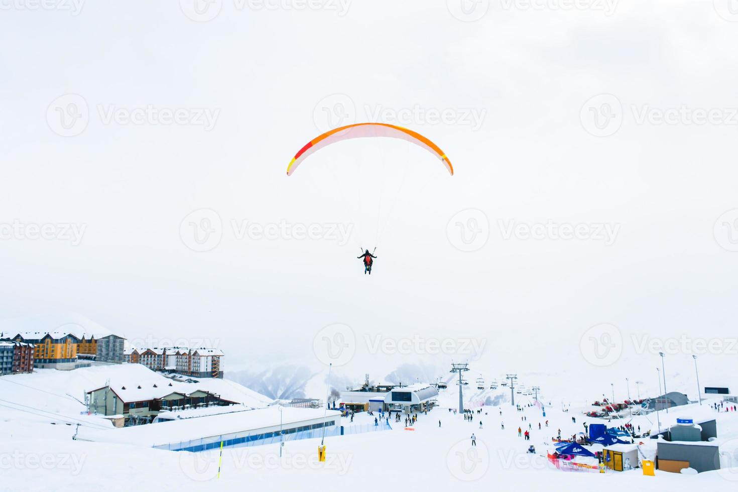 panorama de la station de ski de gudauri avec des parapentes en tandem survolant les skieurs de la station de ski par une froide journée d'hiver photo