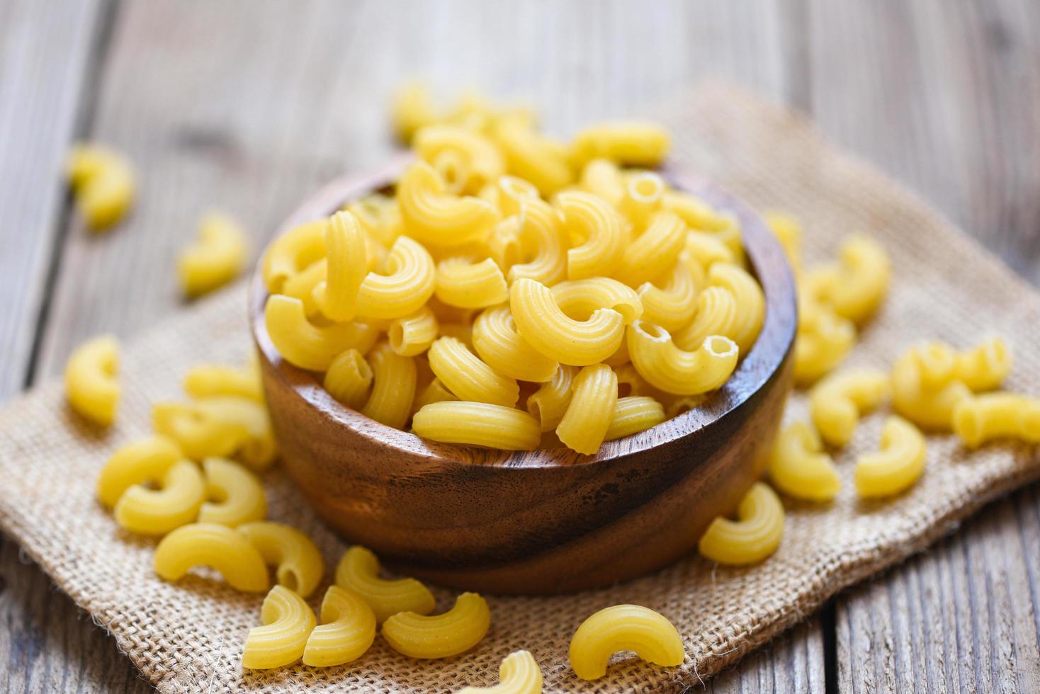 Vue de dessus de macaronis sur fond de bol en bois - gros plan de macaronis crus de délicieuses pâtes ou nouilles penne photo