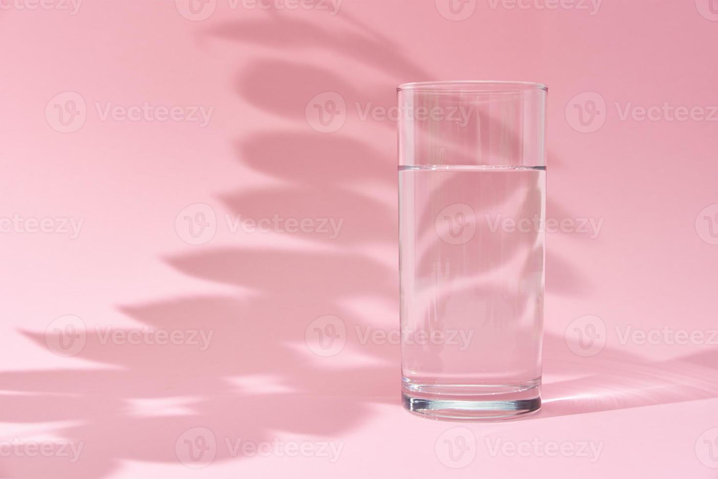 verre d'eau et ombre de feuilles sur fond rose photo