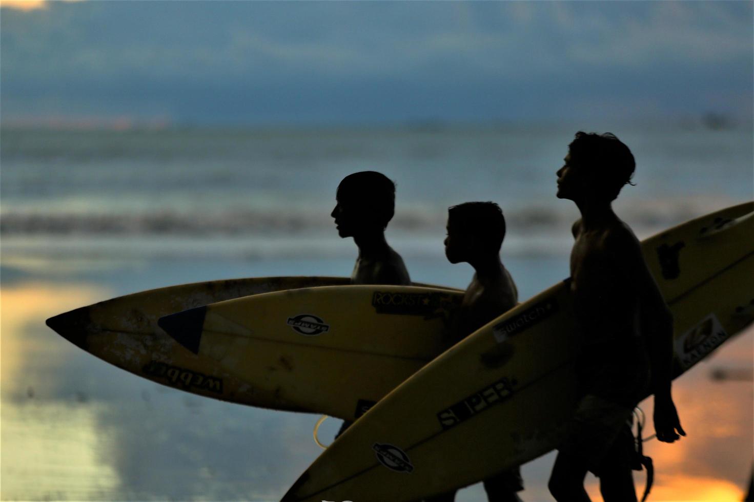 enfants marchant avec une planche de surf avant le coucher du soleil photo