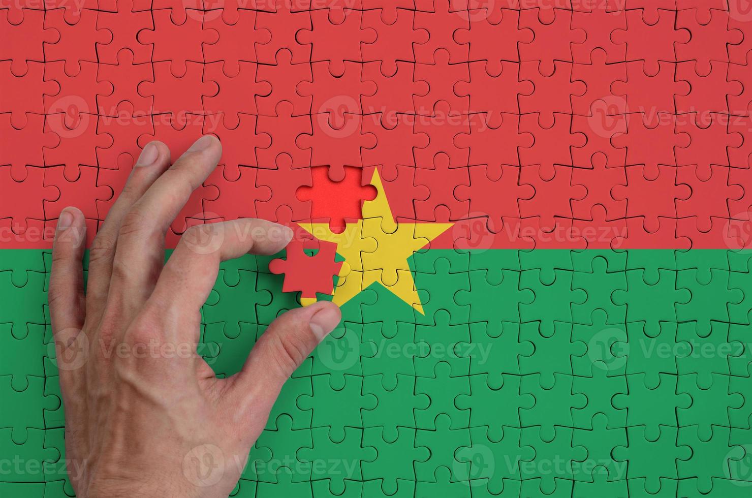 le drapeau du burkina faso est représenté sur un puzzle, que la main de l'homme complète pour se plier photo
