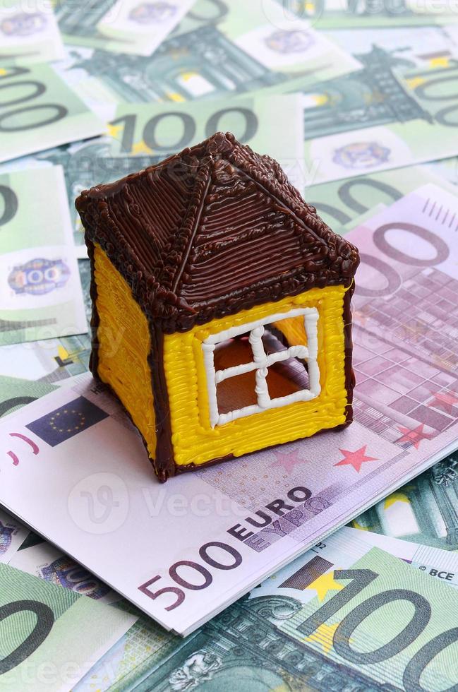 la petite maison de jouets repose sur un ensemble de coupures monétaires vertes de 100 euros. beaucoup d'argent forme un tas infini photo