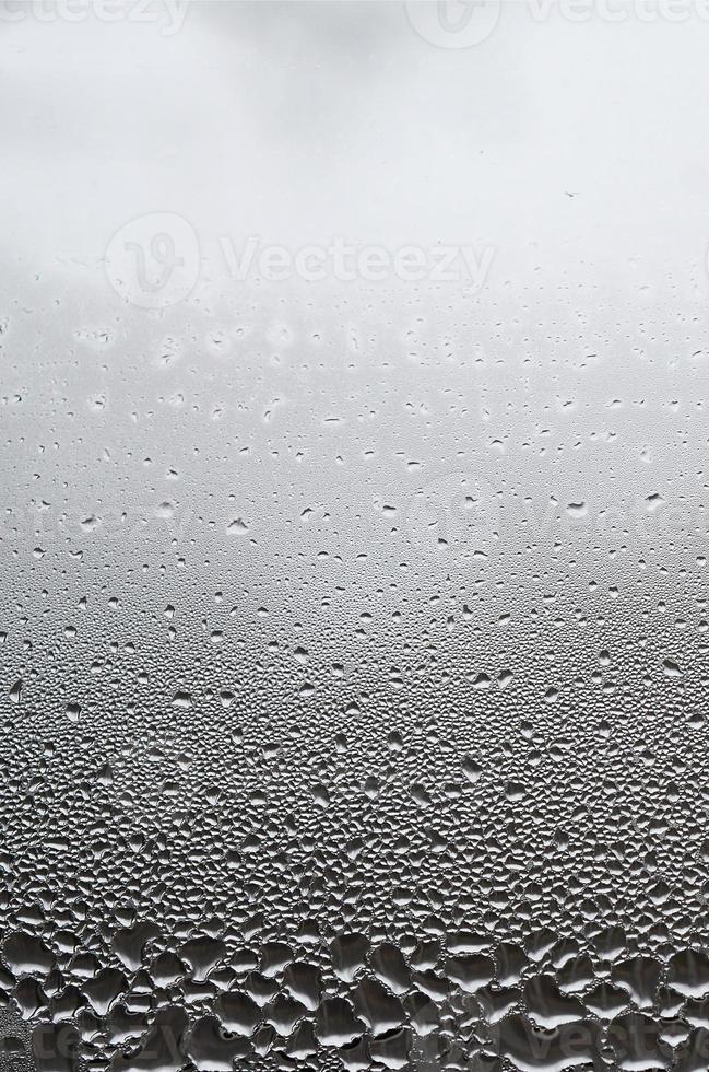 une photo de la surface vitrée de la fenêtre, recouverte d'une multitude de gouttelettes de différentes tailles. texture de fond d'une couche dense de condensat sur verre