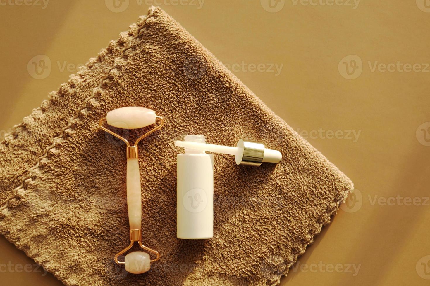 ensemble pour les soins du visage à domicile sur une serviette marron. rouleau de massage facial au quartz rose ou gua sha et sérum dans une bouteille en verre blanc et une pipette pour les soins du visage. kit lifting cosmétique, anti-âge. photo