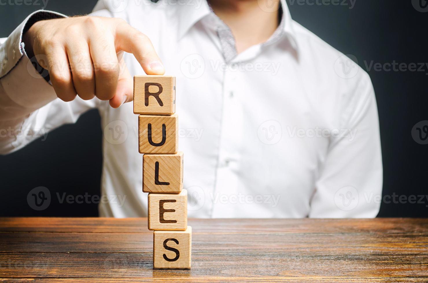 un homme tient une tour de blocs avec le mot règles de tomber. établir des règles et des restrictions claires. direction et rigueur. autoritarisme, cadre de contrôle strict. normes et lois dans la société photo