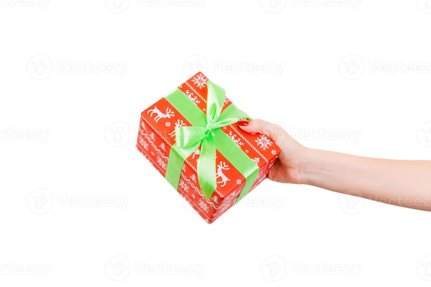 les mains de la femme donnent un noël enveloppé ou d'autres vacances faites à la main dans du papier rouge avec un ruban vert. isolé sur fond blanc, vue de dessus. concept de boîte-cadeau d'action de grâces photo