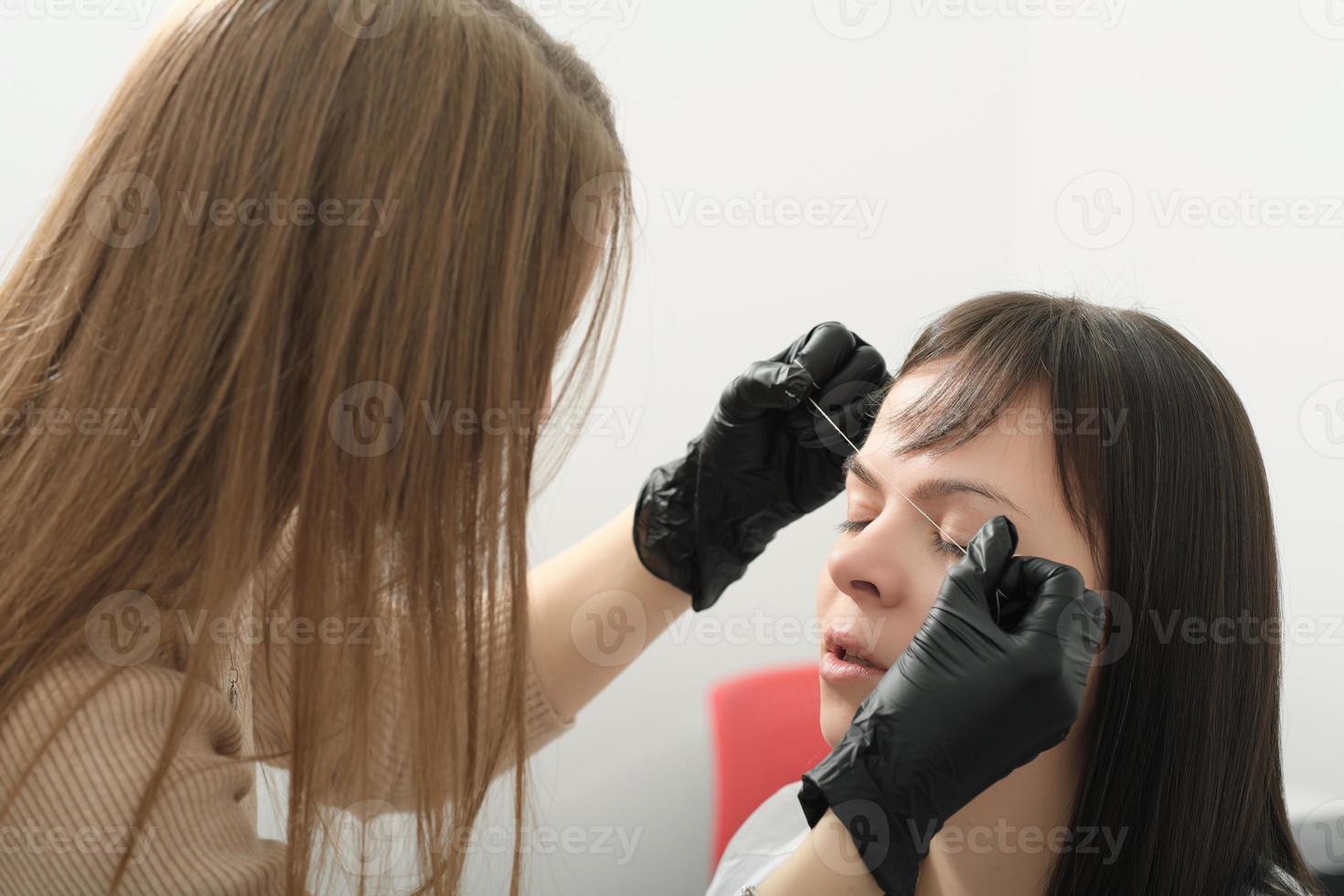 jeune femme pendant la procédure de cartographie professionnelle des sourcils avant le maquillage permanent. esthéticienne faisant le tatouage des sourcils. photo