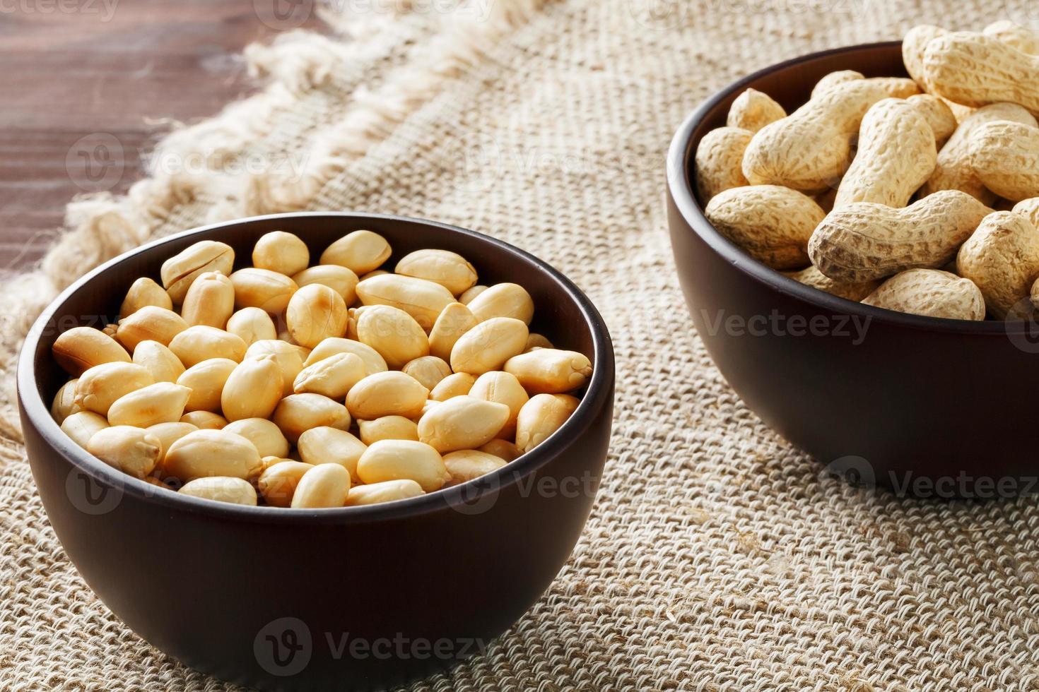 cacahuètes en coque et pelées en gros plan dans des tasses. cacahuètes grillées dans leur coque et épluchées contre un torchon marron. photo