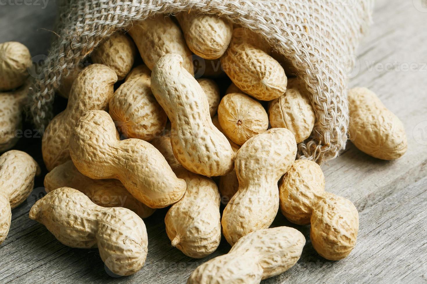 cacahuètes dans un sac de toile de jute miniature sur une vieille surface en bois grise photo