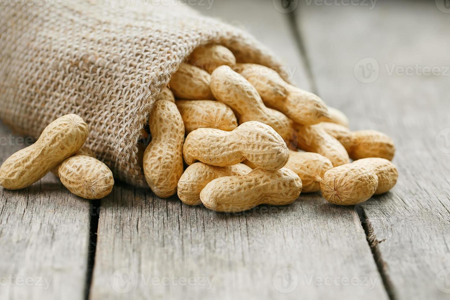 cacahuètes dans un sac de toile de jute miniature sur une vieille surface en bois grise photo