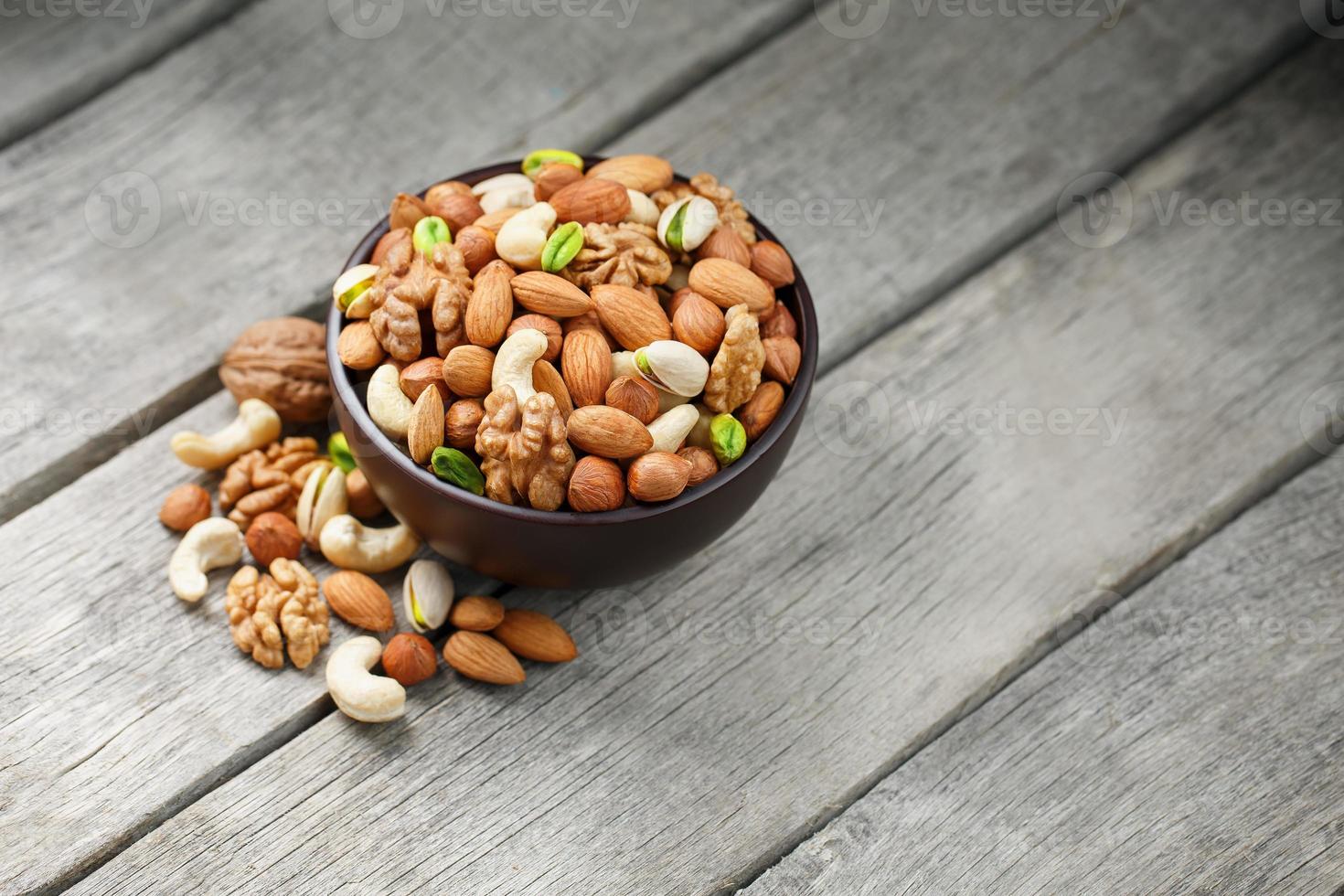 bol en bois avec des noix mélangées sur un fond gris en bois. noix, pistaches, amandes, noisettes et noix de cajou, noix. photo