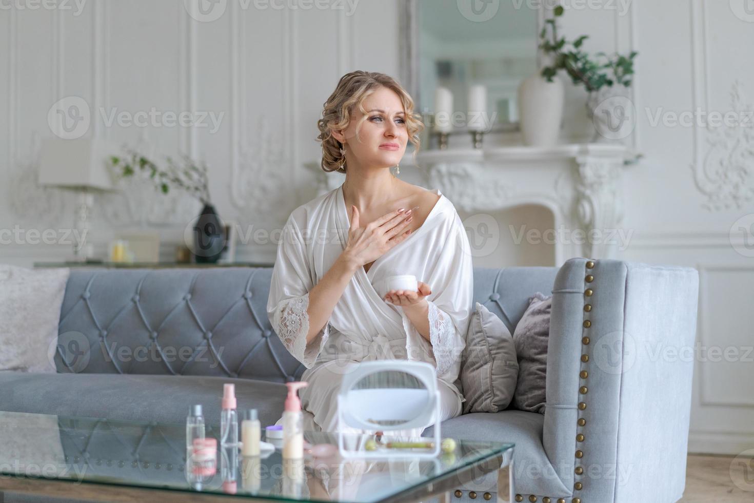 jeune femme heureuse tenant une crème cosmétique pour le visage et souriant tout en appliquant de la crème photo