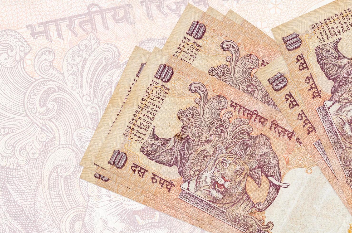 10 billets de roupies indiennes sont empilés sur fond de gros billets semi-transparents. présentation abstraite de la monnaie nationale photo