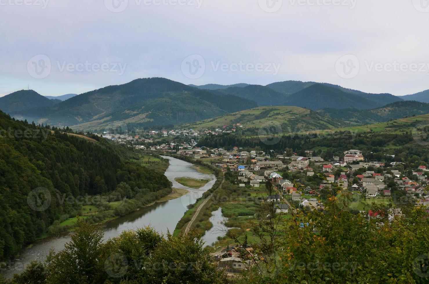 une belle vue sur le village de mezhgorye, région des carpates. beaucoup de bâtiments résidentiels entourés de hautes montagnes forestières et d'une longue rivière photo