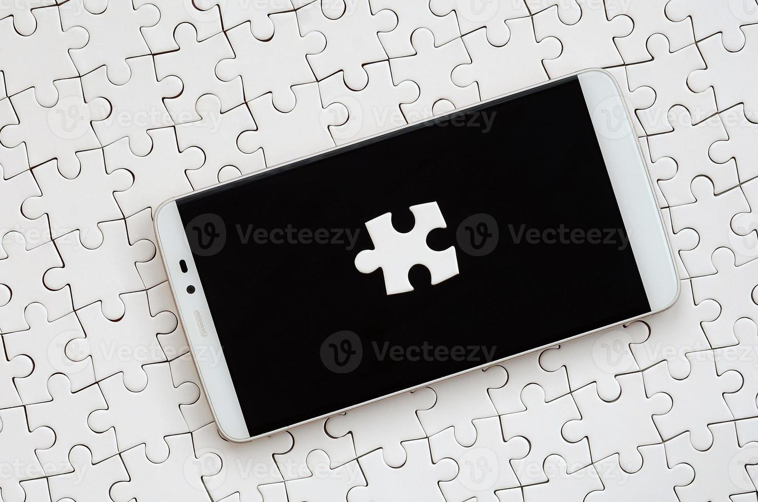 un grand smartphone moderne avec plusieurs éléments de puzzle sur l'écran tactile se trouve sur un puzzle blanc à l'état assemblé photo