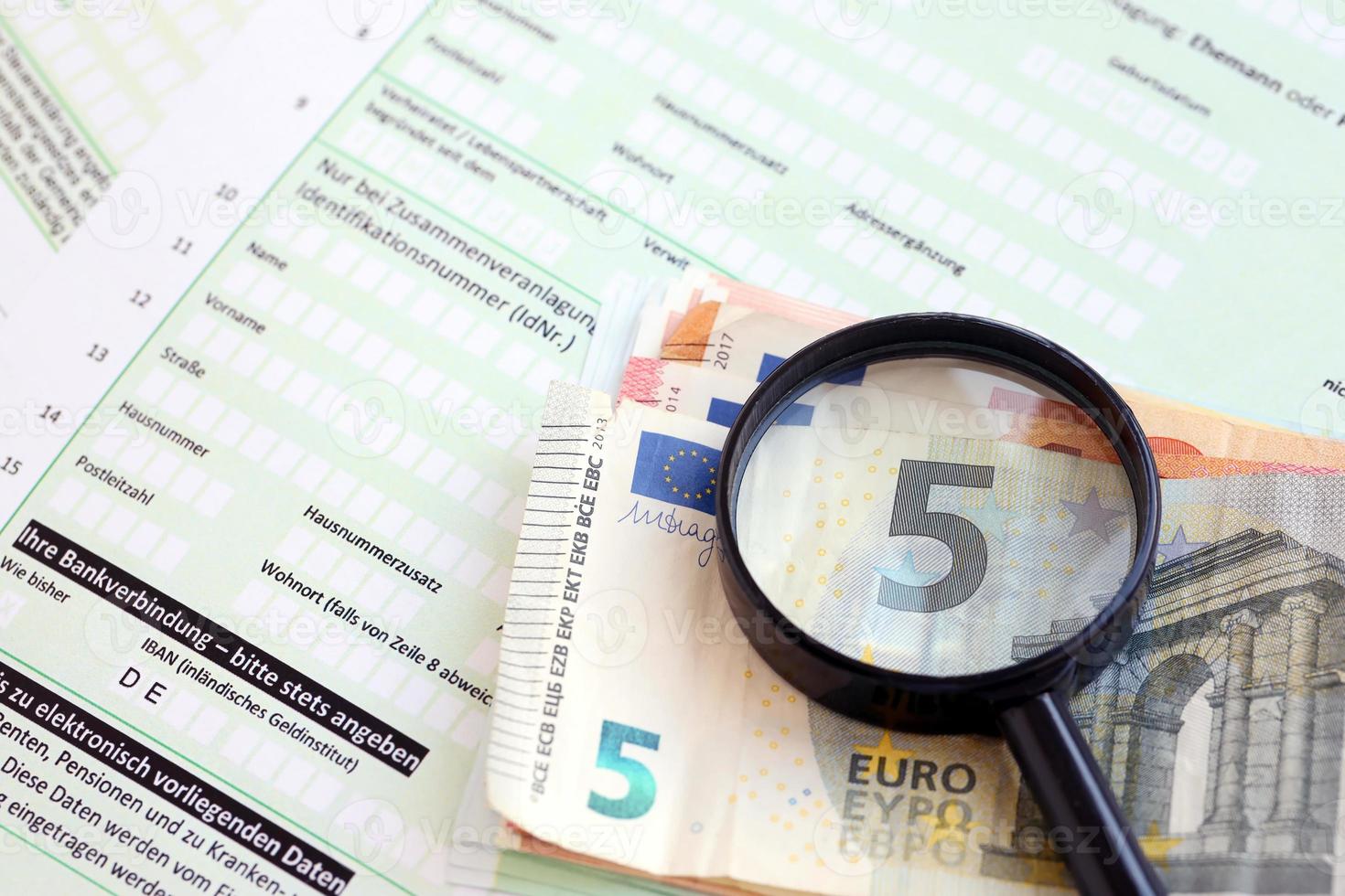 Formulaire de déclaration de revenus allemand avec loupe et factures d'argent en euros européens se trouve sur la table du comptable de près. contribuables allemands utilisant l'euro pour payer leurs impôts photo