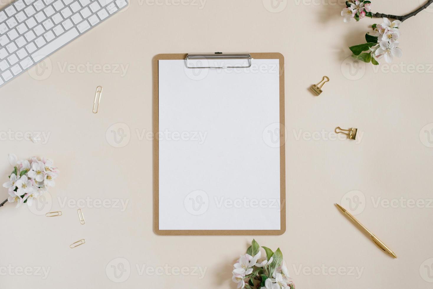 Presse-papiers avec espace copie vierge et fleurs de pomme blanches, clavier, stylo et trombones sur fond beige. mise à plat, modèle de vue de dessus. bureau femme photo