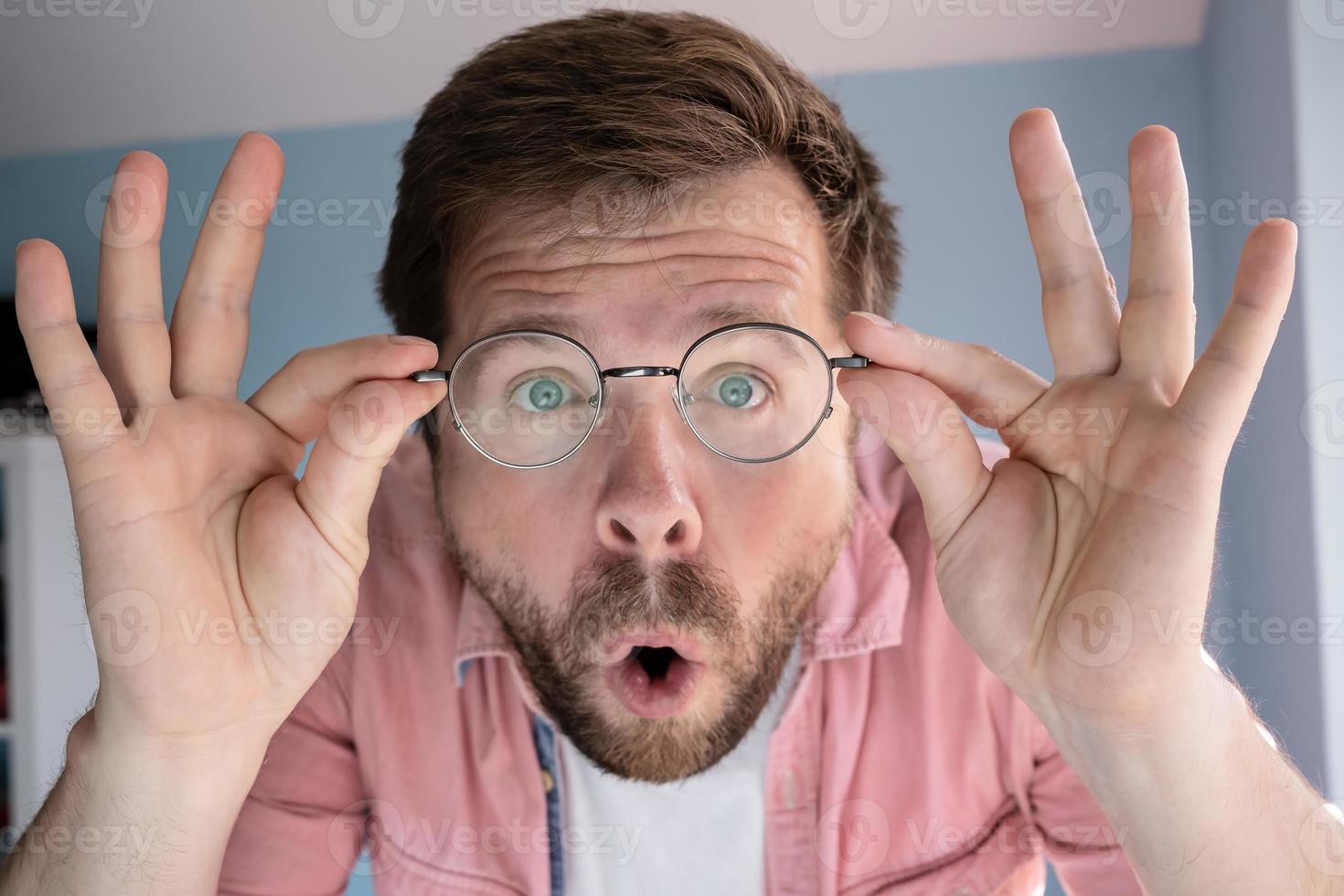 l'homme est étonné, il n'en croit pas les yeux, tient ses lunettes avec les mains et ouvre la bouche de surprise. fermer. photo