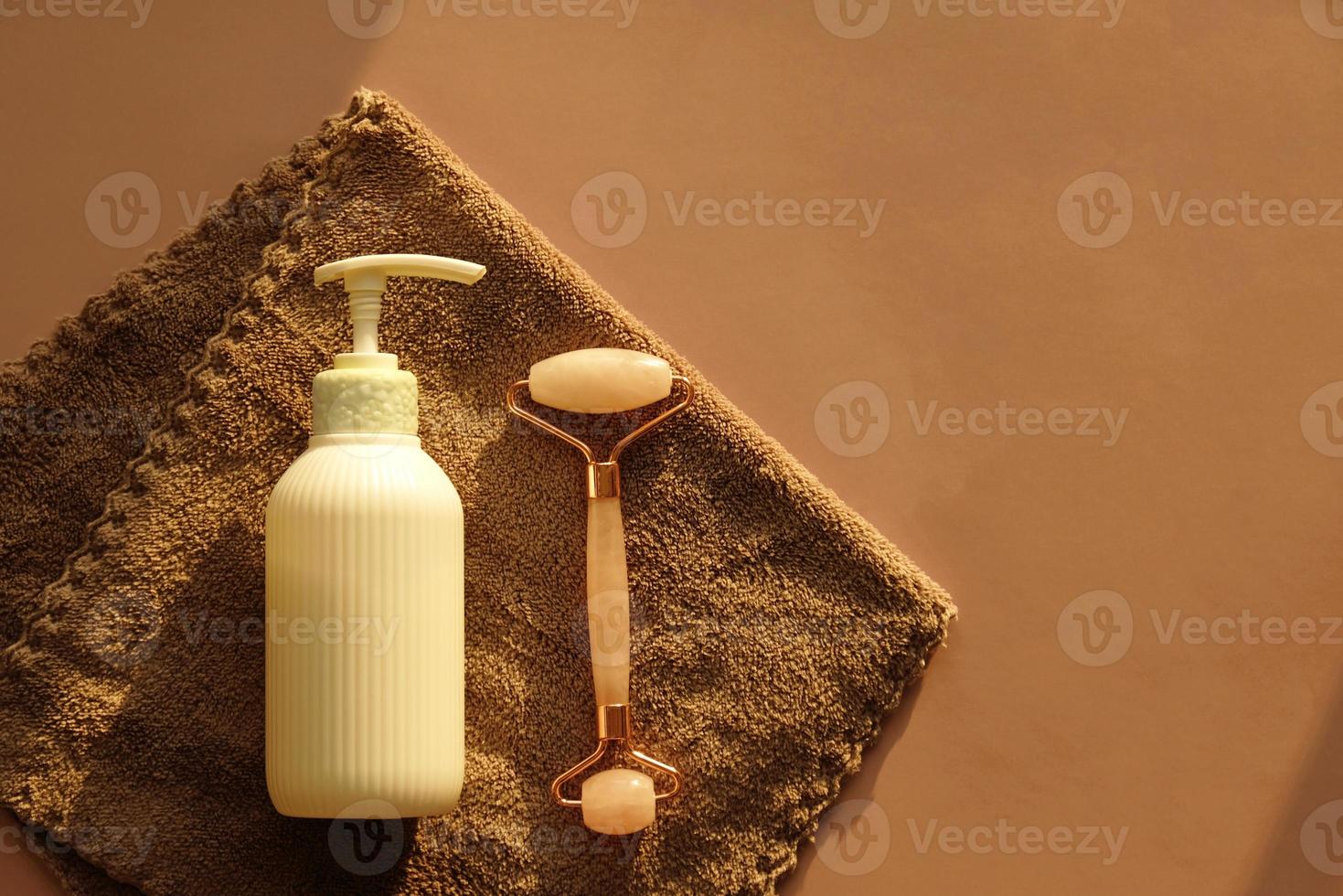 ensemble pour les soins du visage à domicile sur une serviette marron. rouleau de massage facial au quartz rose ou gua sha et sérum dans une bouteille en verre blanc et une pipette pour les soins du visage. kit lifting cosmétique, anti-âge. photo