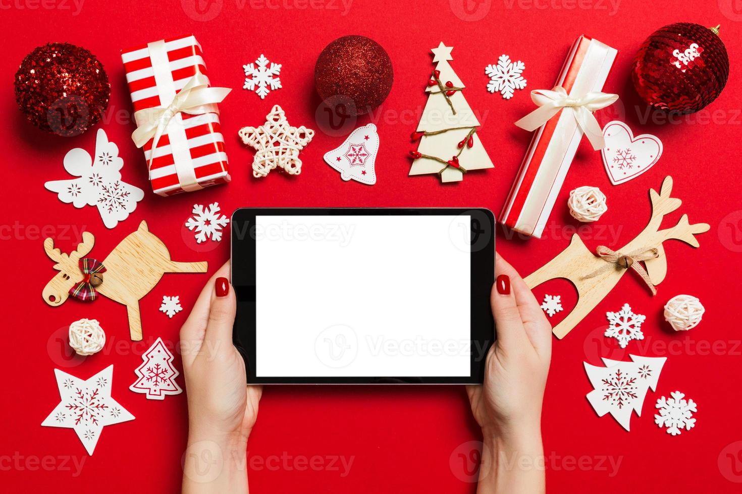 vue de dessus d'une femme tenant une tablette dans ses mains sur fond rouge fait de décorations de noël. concept de vacances du nouvel an. maquette photo