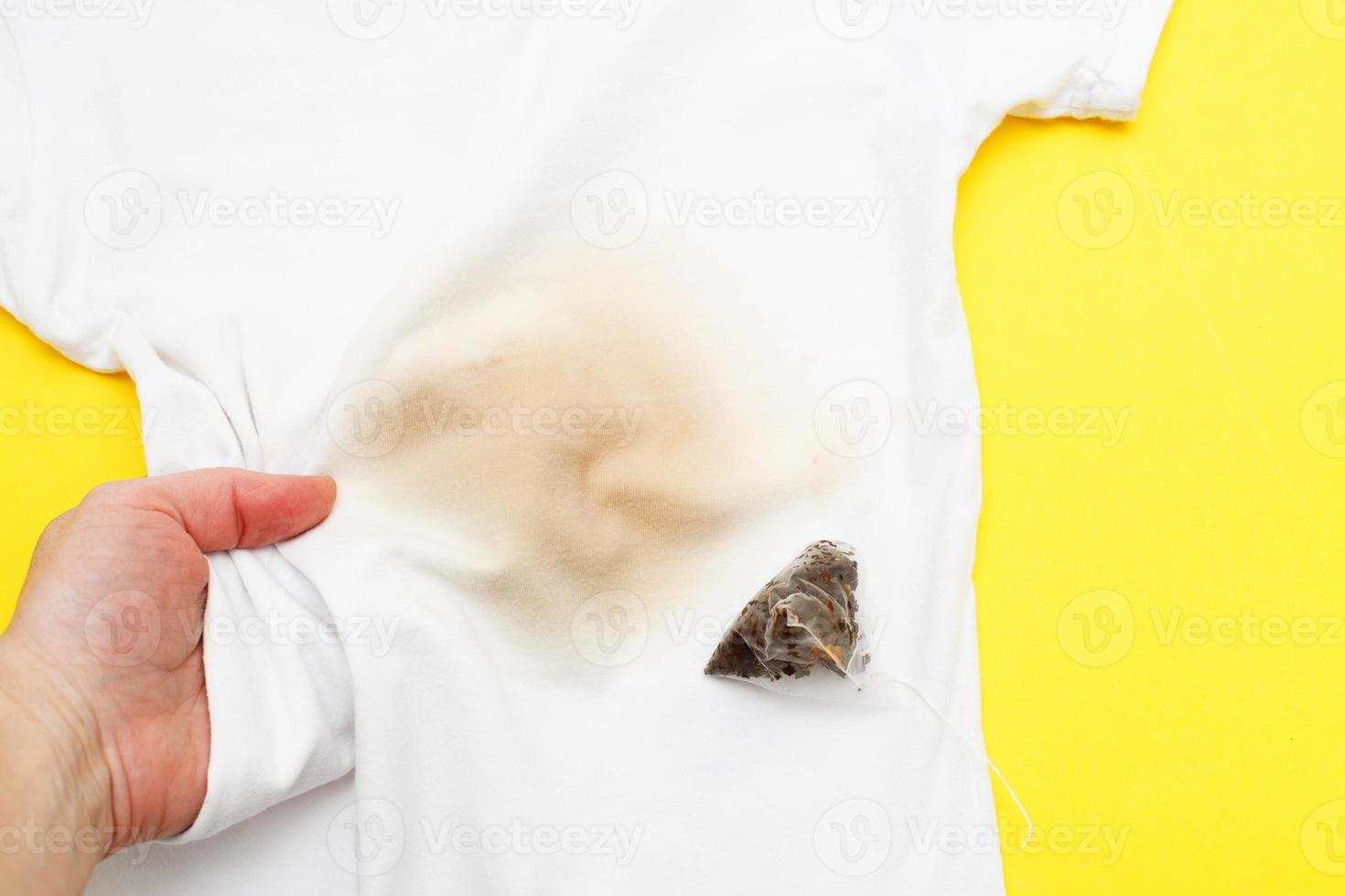 main féminine tenant des vêtements blancs avec une tache de thé sale avec un sachet de thé à côté photo