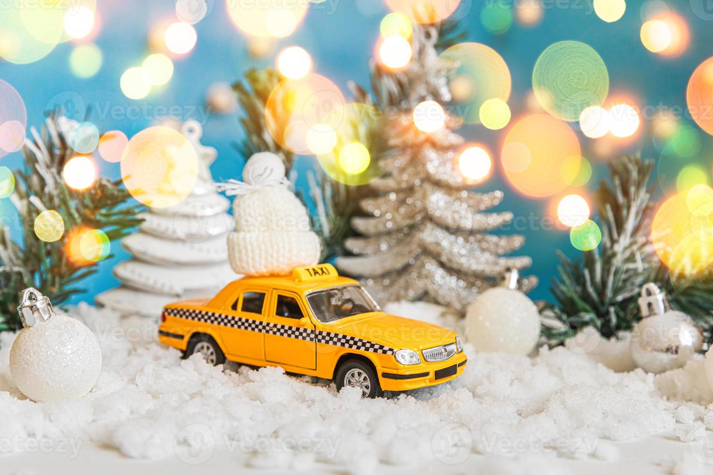 fond de bannière de Noël. modèle de taxi de voiture de jouet jaune et ornements de décorations d'hiver sur fond bleu avec de la neige et des lumières de guirlande défocalisées. concept de service de taxi de livraison de trafic urbain. photo