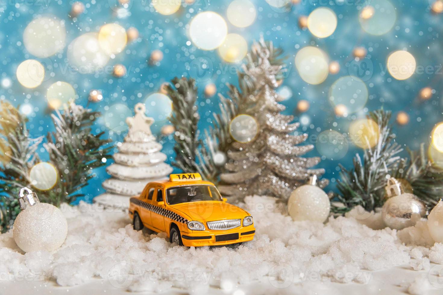 fond de bannière de Noël. modèle de taxi de voiture de jouet jaune et ornements de décorations d'hiver sur fond bleu avec de la neige et des lumières de guirlande défocalisées. concept de service de taxi de livraison de trafic urbain. photo