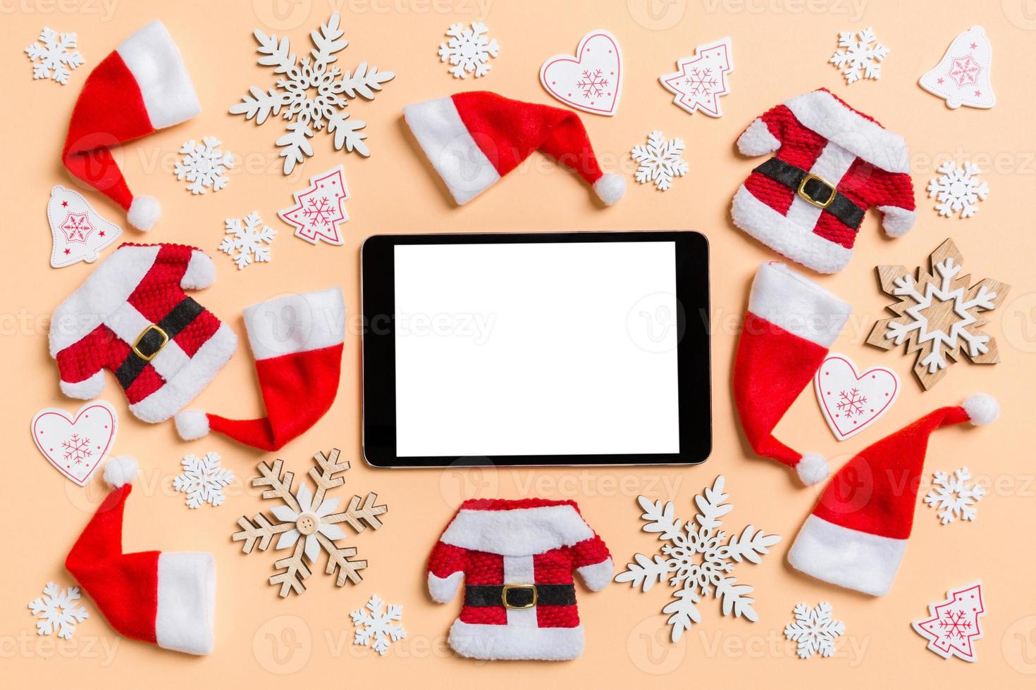 vue de dessus de la tablette numérique avec des décorations de noël et des chapeaux de père noël sur fond orange. concept de joyeuses fêtes photo