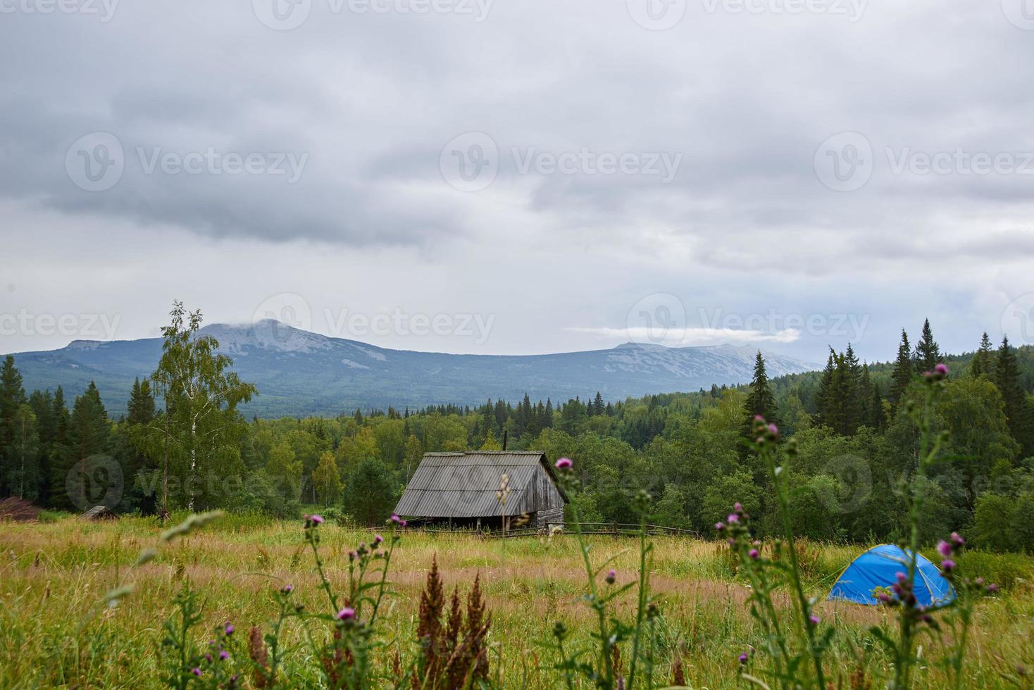 paysage, pré vert, tente bleue, maison en bois, herbes des champs, belle vue sur les sommets des montagnes dans les nuages. photo