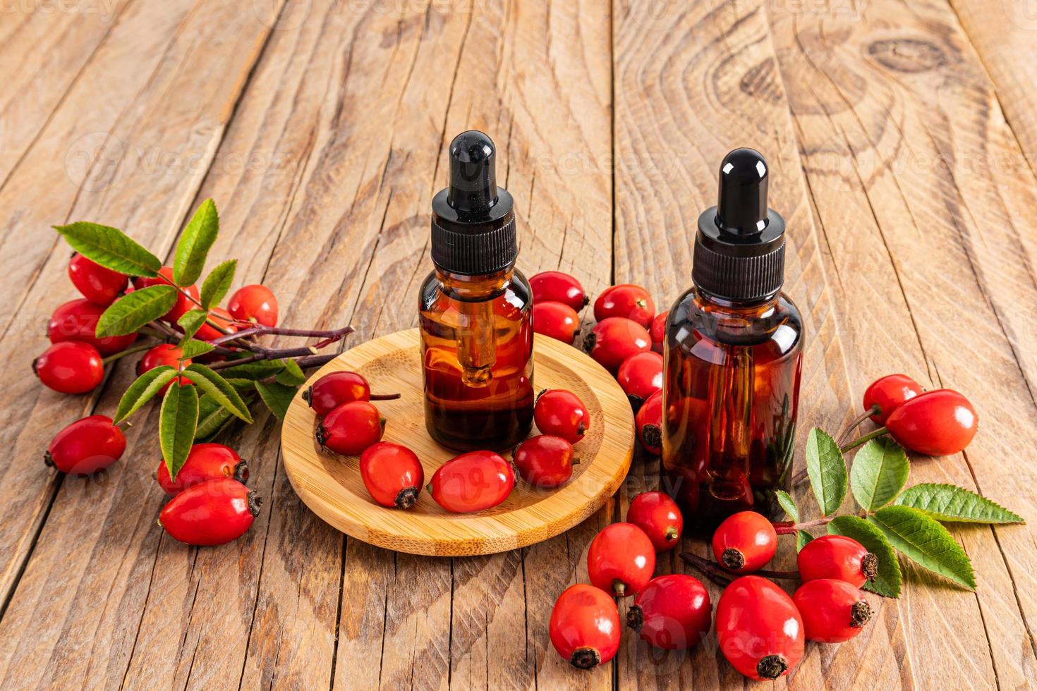 deux bouteilles cosmétiques avec une pipette avec un produit biologique à base d'huile de graines de rose musquée sur un fond en bois parmi les baies de rose musquée mûres. vue de face. photo