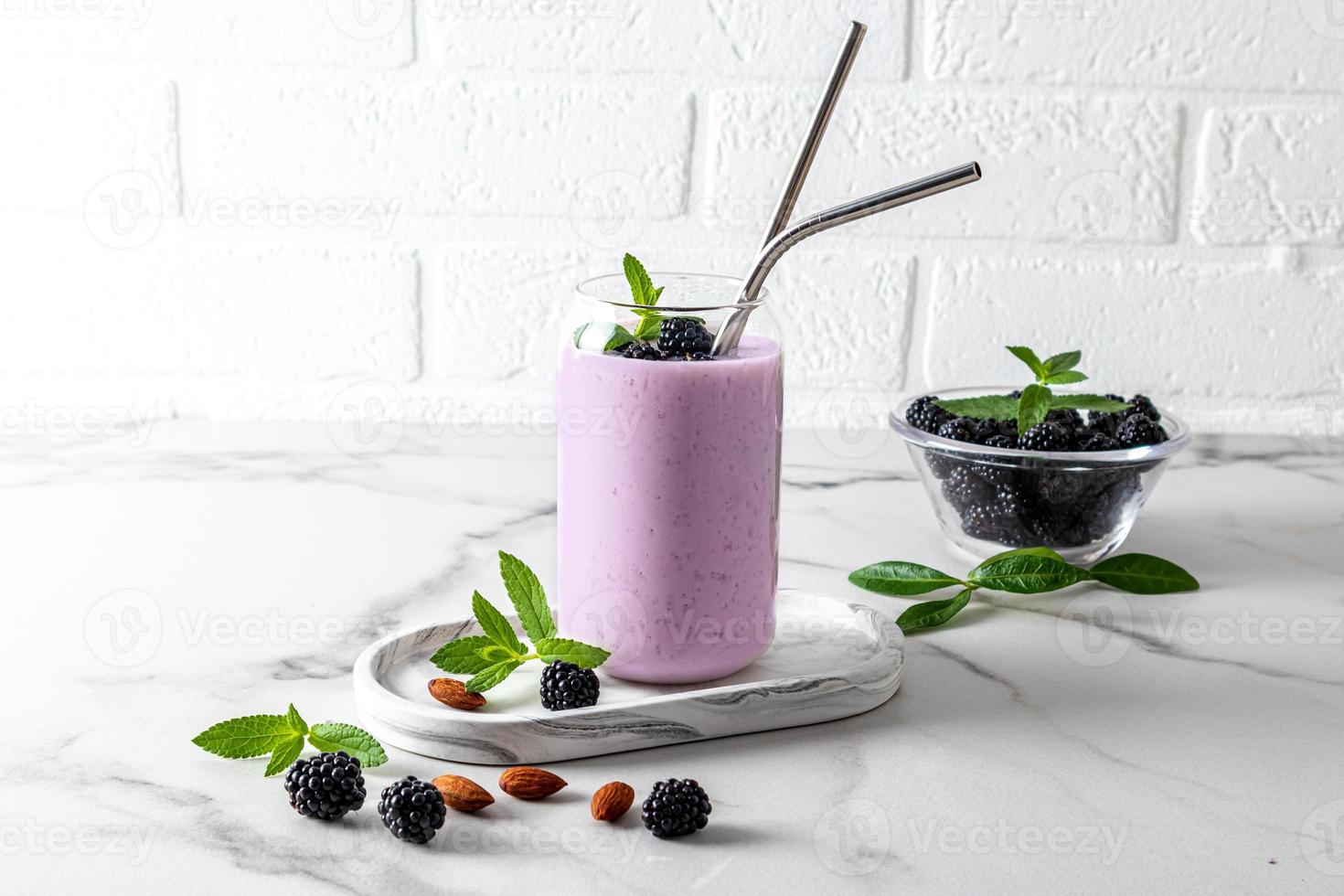 cocktail ou smoothie aux baies de mûre dans des verres en verre modernes en forme de canette de bière avec de la paille écologique en face d'un mur de briques blanches. alimentation équilibrée. photo