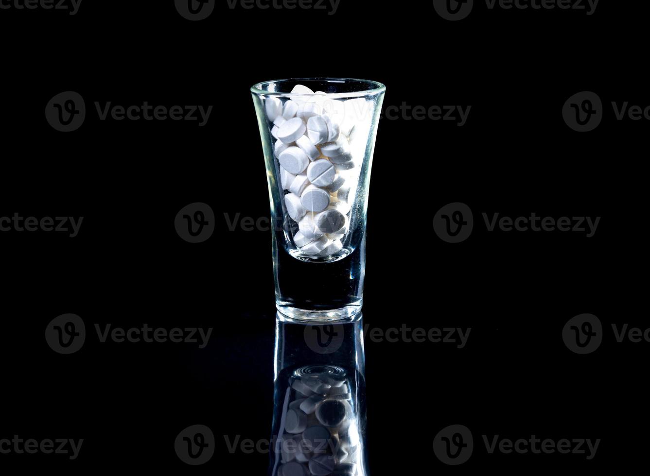 pilules oranges blanches dans un verre à vin. en pot. dans un seau isolé sur un ensemble noir de capsules et de pilules à l'intérieur de gros plan, photo