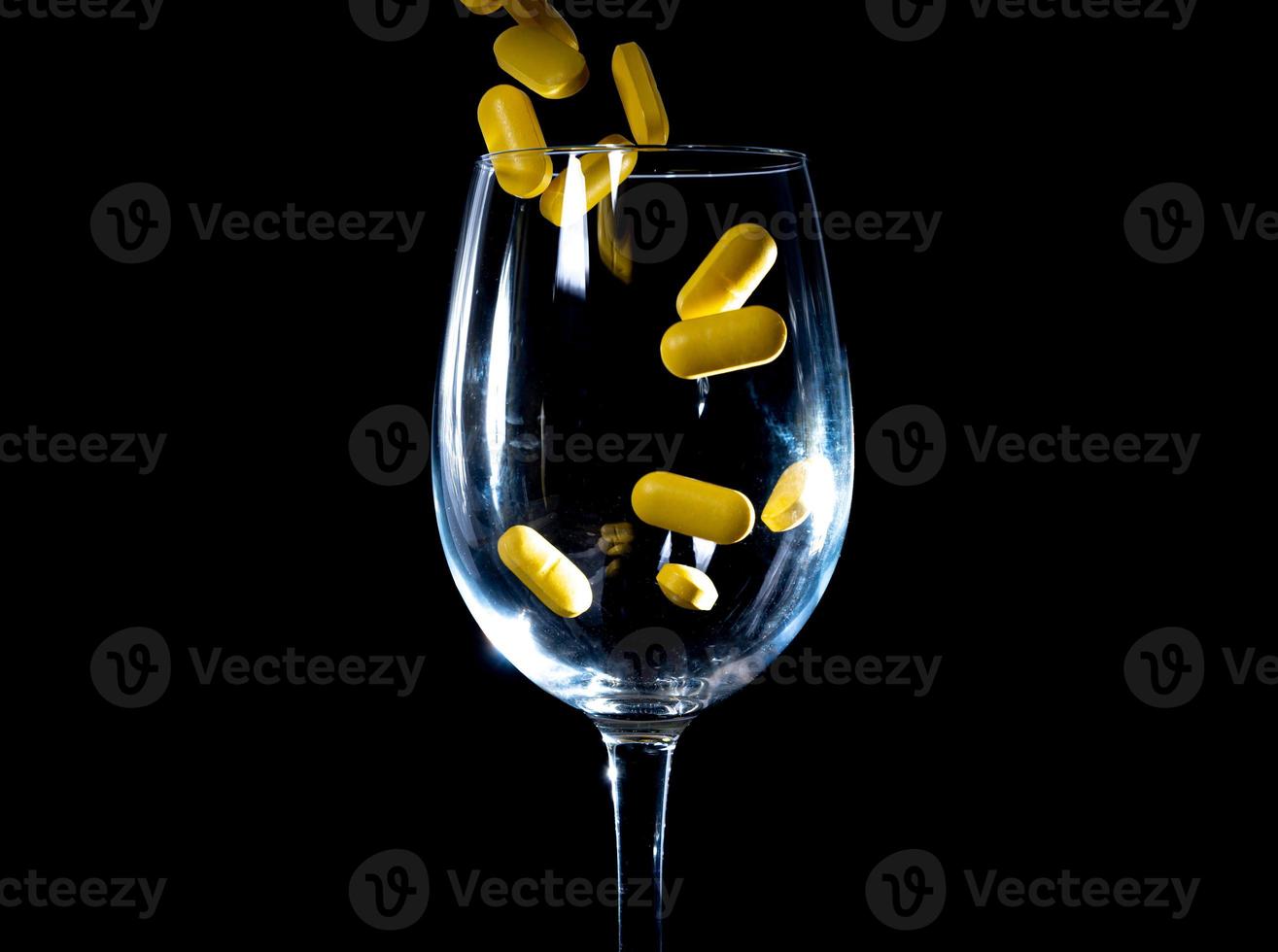 pilules oranges blanches dans un verre à vin. en pot. dans un seau isolé sur un ensemble noir de capsules et de pilules à l'intérieur de gros plan, photo