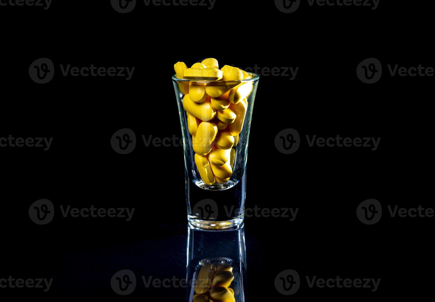 pilules oranges blanches dans un verre à vin. en pot. dans un seau isolé sur un ensemble noir de capsules et de pilules à l'intérieur de gros plan, photo