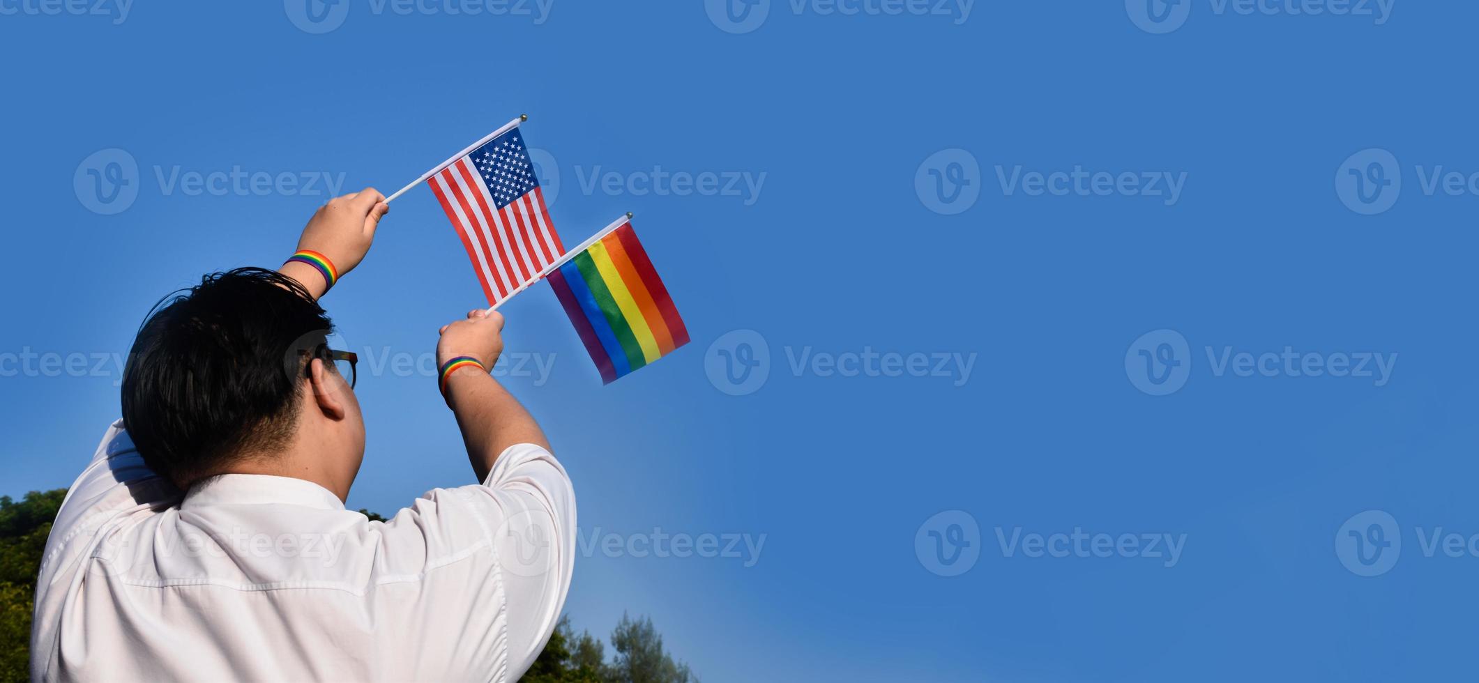 drapeau américain et drapeau arc-en-ciel levant dans les mains et contre le ciel bleu, mise au point douce et sélective, concept pour les célébrations lgbt et les événements lgbt dans le mois de la fierté aux états-unis. photo