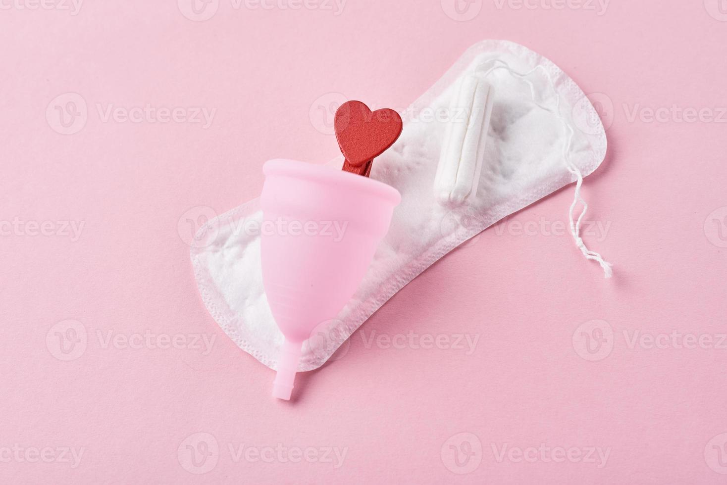 serviette hygiénique, coupe menstruelle, tampon et coeur en bois rouge sur fond rose photo