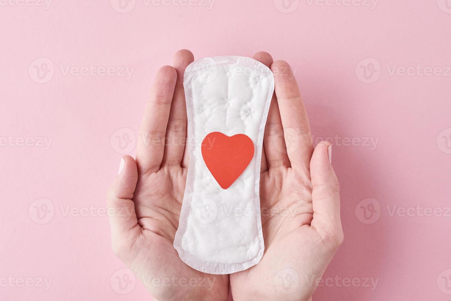les mains d'une femme tiennent une serviette hygiénique avec un coeur rouge sur fond rose photo