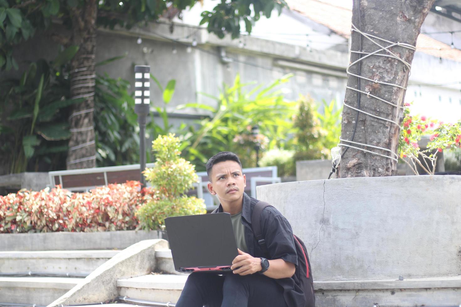 jeune homme asiatique séduisant utilisant un ordinateur portable confus dans un espace de travail partagé avec un visage malheureux photo