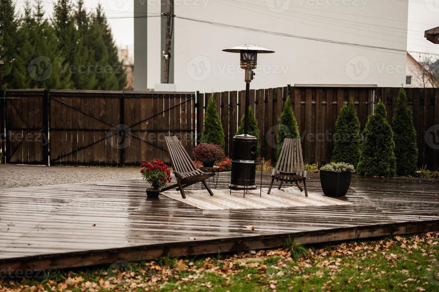 chauffe-terrasse extérieur à gaz en acier inoxydable avec chaises en bois et pot de fleurs sur terrasse humide. endroit pour se détendre. photo