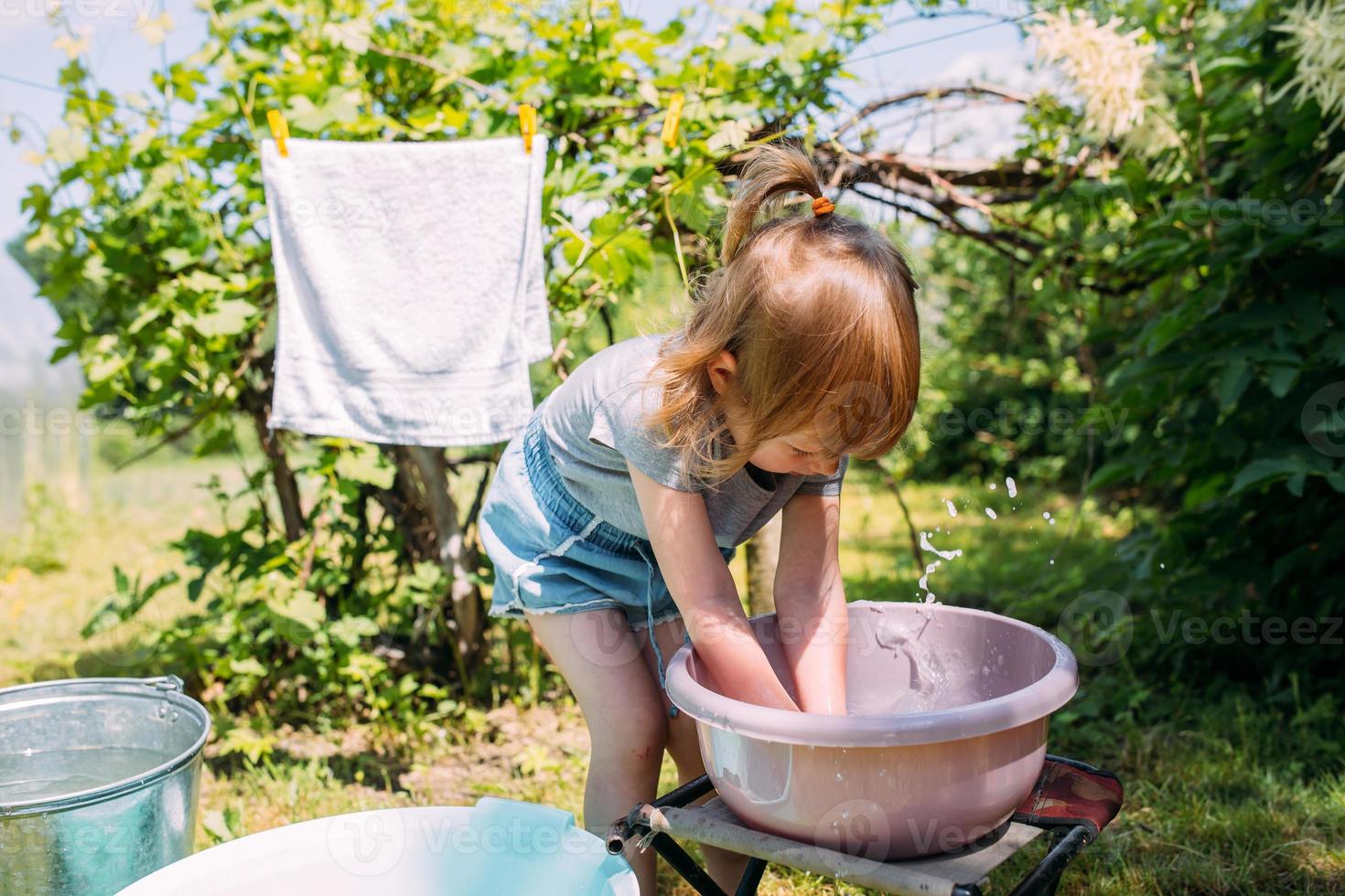 petite fille d'âge préscolaire aide à faire la lessive. enfant lave les vêtements dans le jardin photo