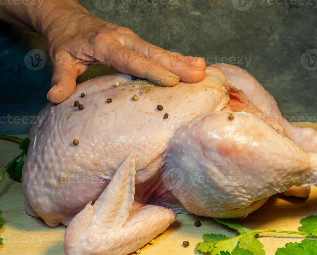 frotter le poulet avec du poivre. frotter le poulet au poivre. poivrer la viande. la préparation des aliments. appliquer des épices sur un poulet entier photo