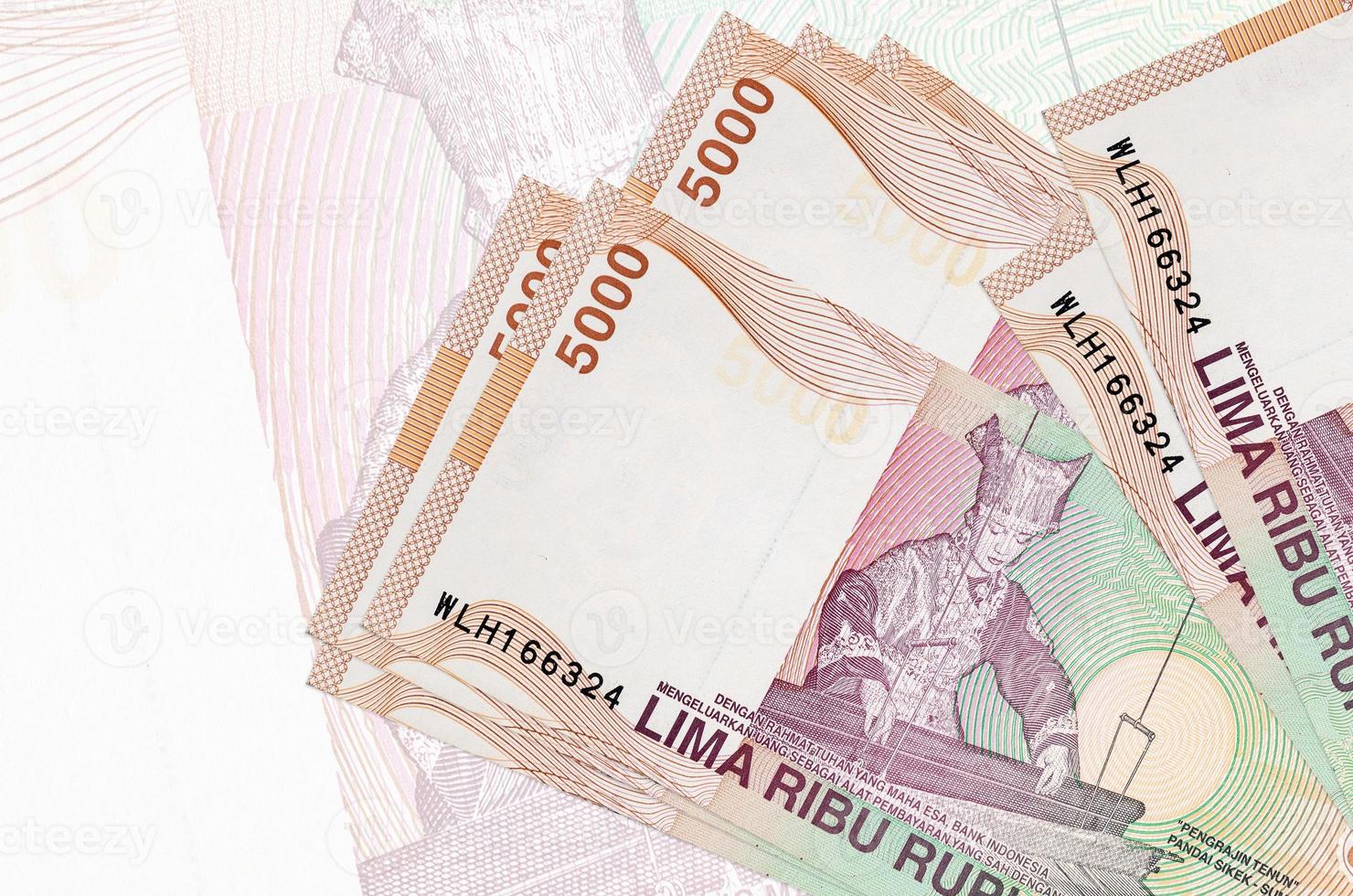 Les billets de 5000 roupies indonésiennes sont empilés sur fond de gros billets de banque semi-transparents. présentation abstraite de la monnaie nationale photo