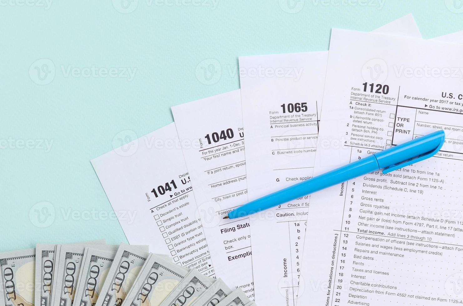 les formulaires fiscaux se trouvent près de billets de cent dollars et d'un stylo bleu sur fond bleu clair. déclaration d'impôt sur le revenu photo