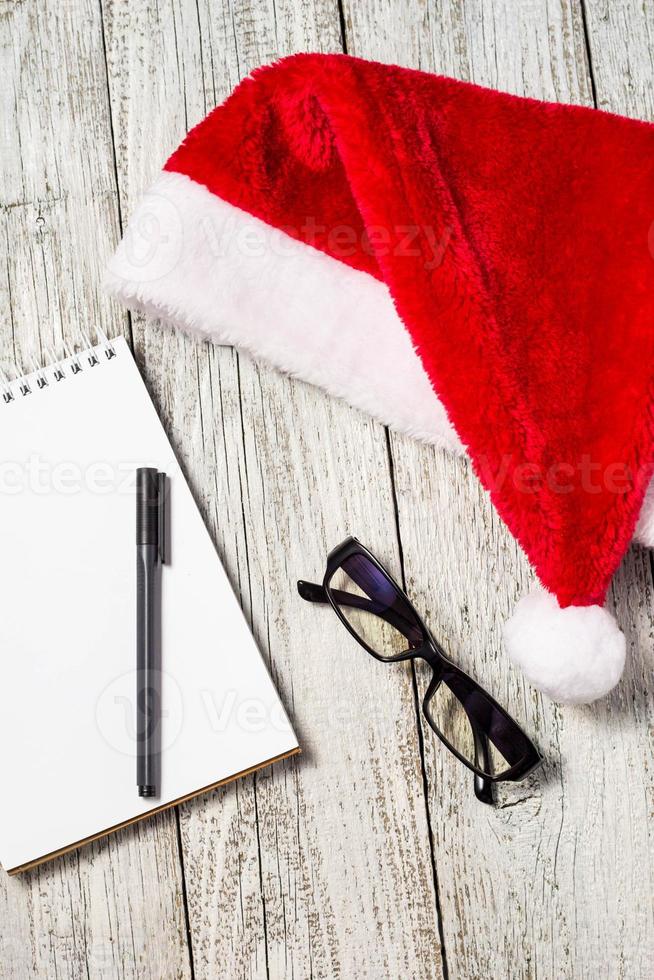 fond de noël et du nouvel an avec bonnet rouge, lunettes, bloc-notes et stylo pour vos souhaits photo