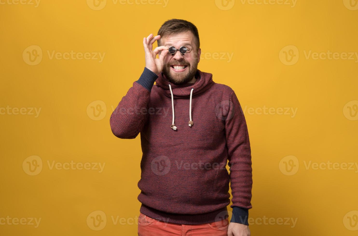 un homme barbu caucasien joyeux tient des lunettes de soleil jouets comme un pince-nez à ses yeux, avec une grimace et un sourire bizarres. fond jaune. photo