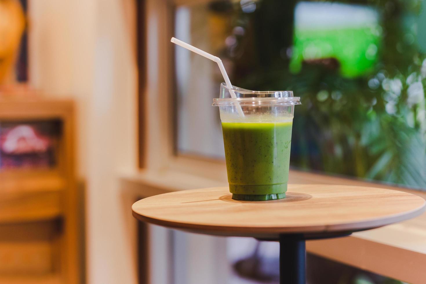 smoothie vert en verre plastique avec paille sur table en bois au café. photo
