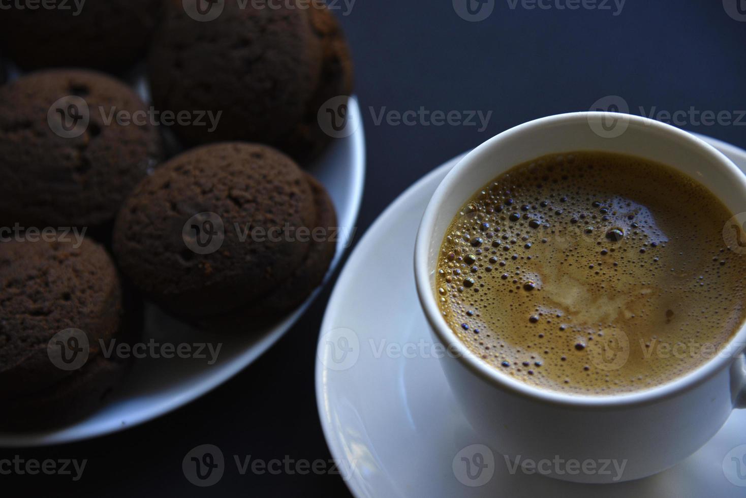 délicieux café noir avec de la mousse dans une tasse blanche avec des biscuits sucrés. délicieux petit déjeuner avec café et biscuits. biscuits sucrés et doux sur fond noir. photo