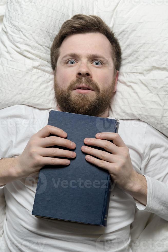 un homme stupéfait est allongé dans son lit, tenant le livre qu'il a terminé sur la poitrine et lève les yeux avec enthousiasme. vue de dessus. photo