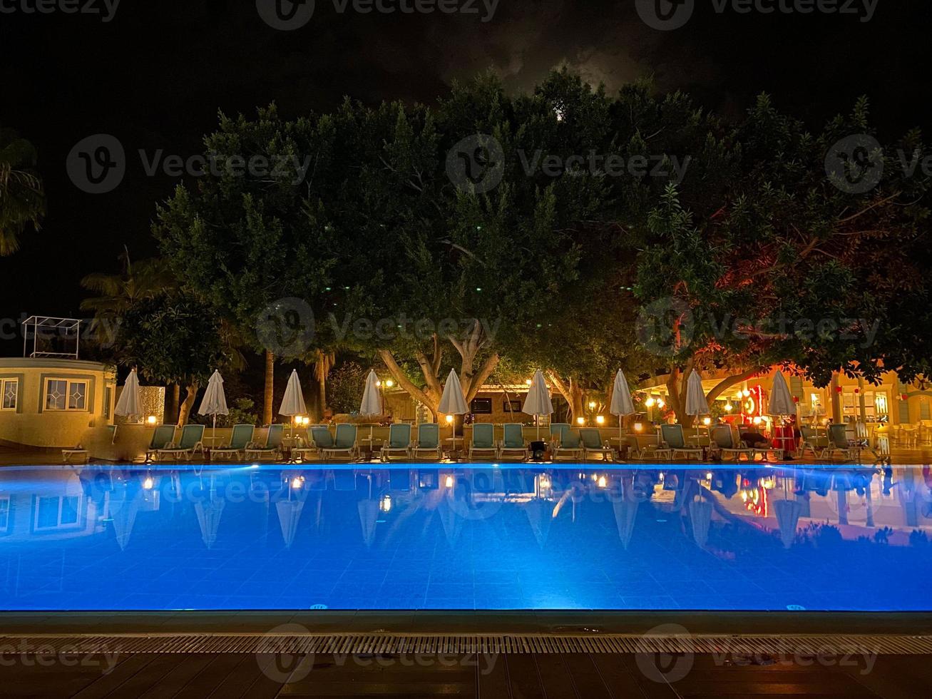 des parasols, des chaises longues et une piscine d'eau chaude et claire à l'hôtel tout compris la nuit dans une station balnéaire tropicale paradisiaque orientale photo